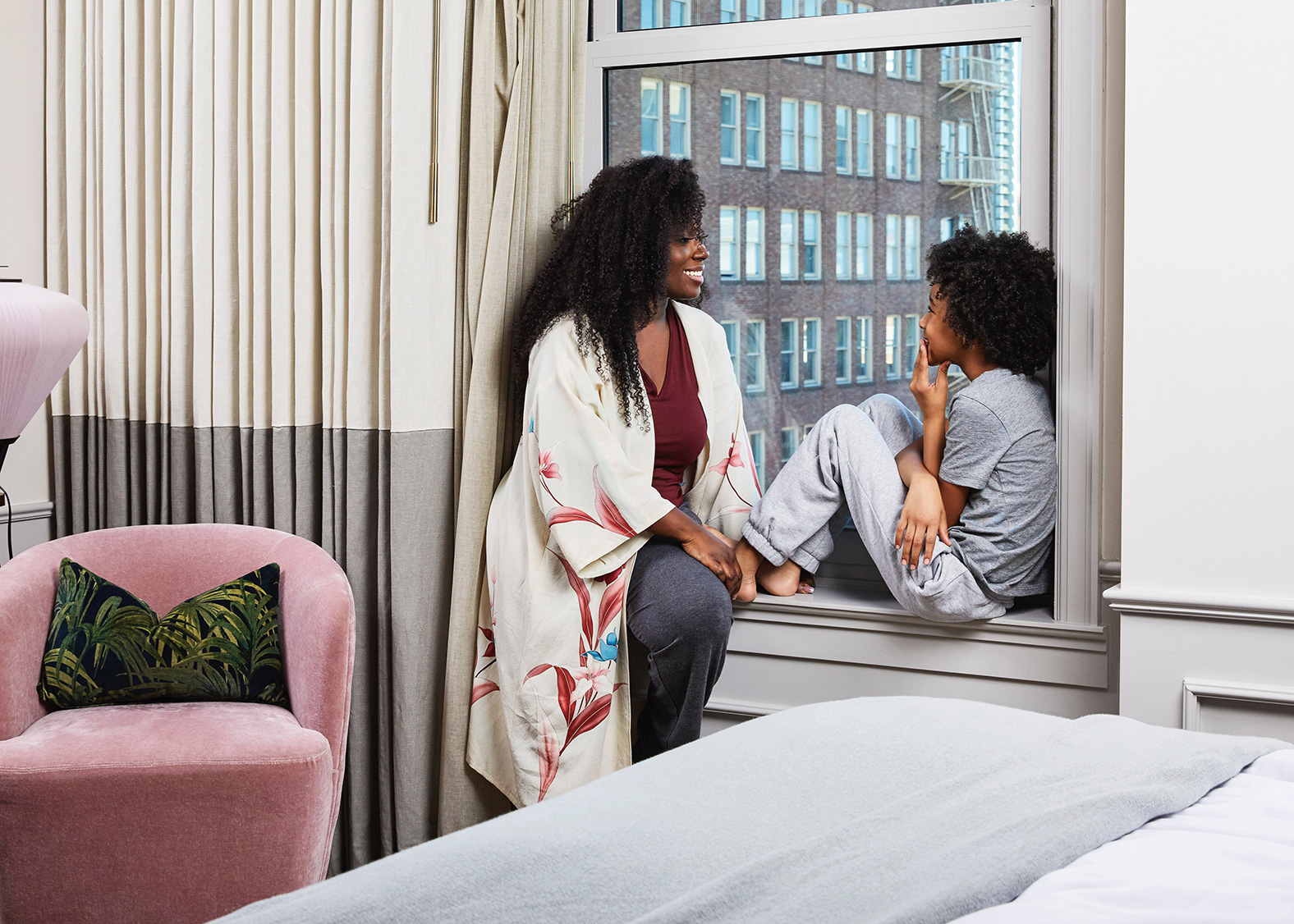 Heartwarming hotel moment captured by Kimberly Genevieve: A joyful mom and son laughing together in a cozy hotel room